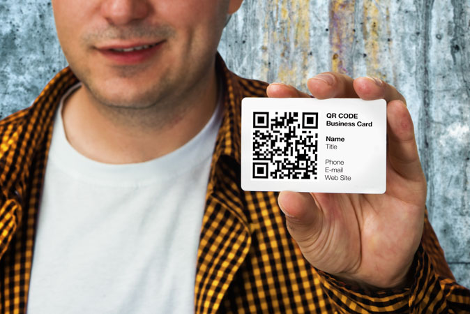 Άντρας κρατά στο χέρι πρωτότυπη επαγγελματική κάρτα με τυπωμένο κωδικό QR.