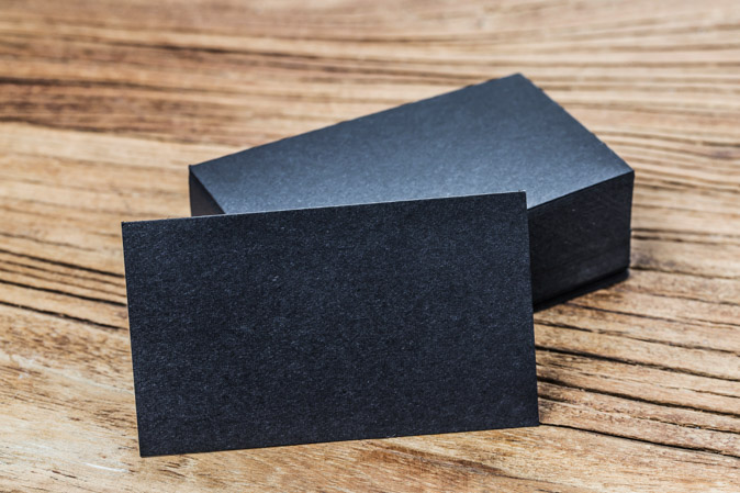Πρωτότυπες μαύρες, ανάγλυφες επαγγελματικές κάρτες στοιβαγμένες πάνω σε ξύλινη επιφάνεια.