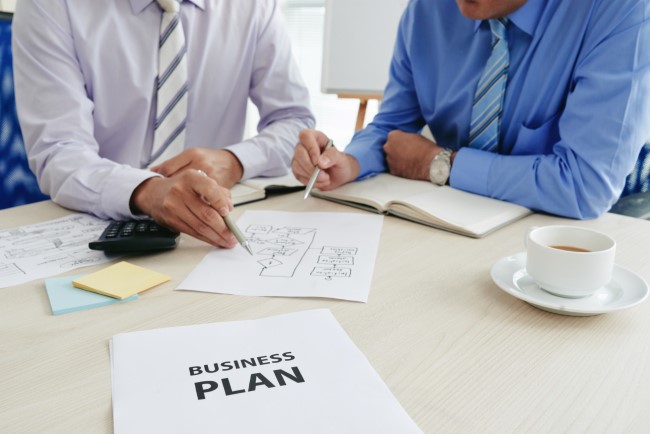 Δύο επίσημα ντυμένοι άντρες προσπαθούν να φτιάξουν ένα επιχειρηματικό σχέδιο (business plan).